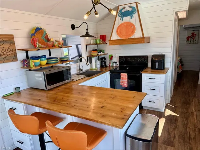 Kitchen with butcher block countertops, white cabinets, wooden walls, stainless steel microwave, and dark wood-type flooring
