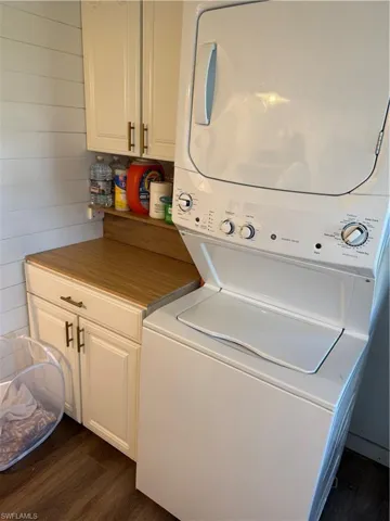 Laundry area featuring cabinet space, stacked washer / drying machine, dark wood-style flooring, and wood walls