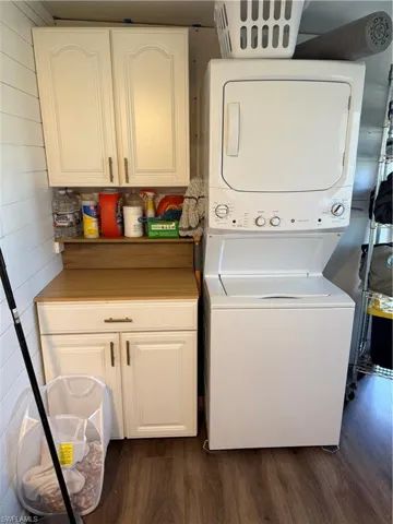Laundry area featuring stacked washing machine and dryer, dark wood-style floors, and cabinet space
