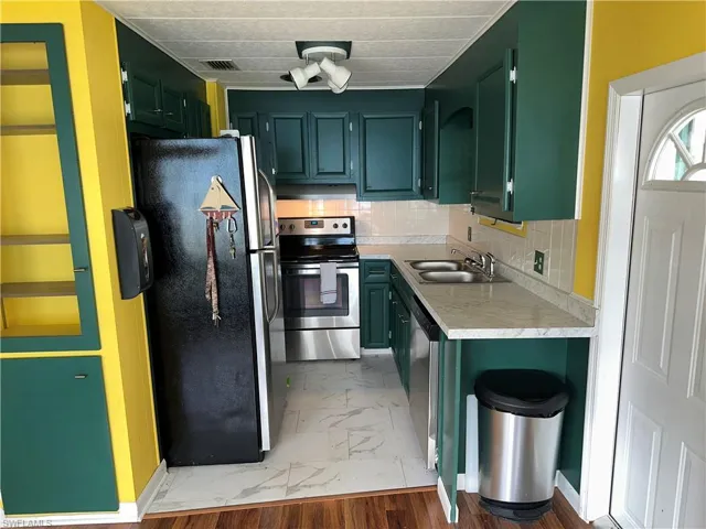 Kitchen featuring appliances with stainless steel finishes, green cabinetry, light countertops, backsplash, and light marble finish flooring