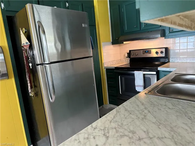 Kitchen with appliances with stainless steel finishes, light countertops, green cabinetry, backsplash, and exhaust hood