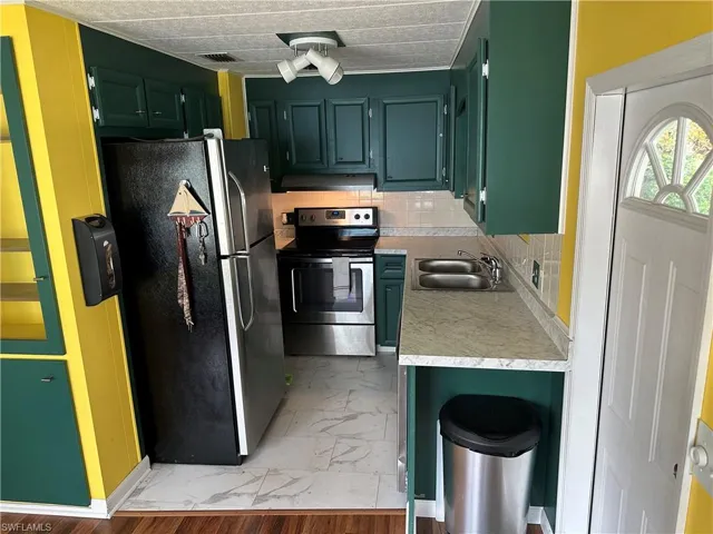 Kitchen with light countertops, stainless steel appliances, backsplash, green cabinets, and under cabinet range hood