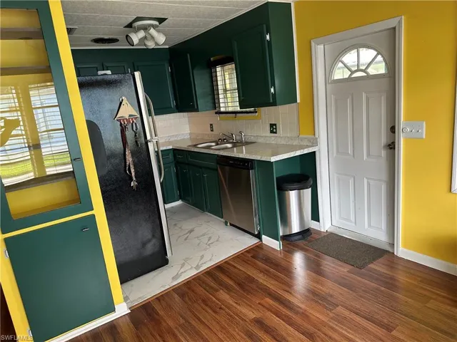 Kitchen featuring green cabinets, light countertops, backsplash, stainless steel appliances, and light wood-type flooring