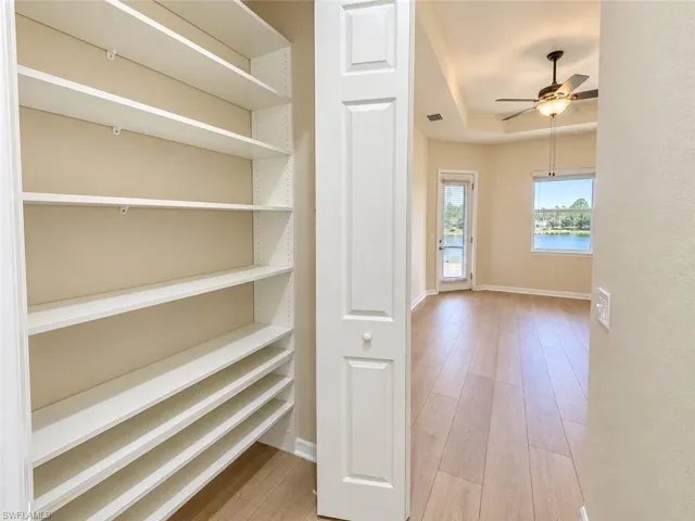 Built-in shelving, wood-finish flooring, tray ceiling, ceiling fan, and a glass-paneled door
