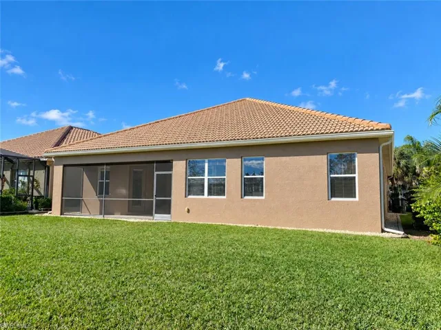 Expansive backyard featuring a manicured lawn, screened patio, stucco exterior, multiple windows, and a tile roof