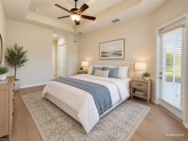 Tray ceiling with a ceiling fan, wood-finish flooring, light-toned walls, and a glass-paneled door