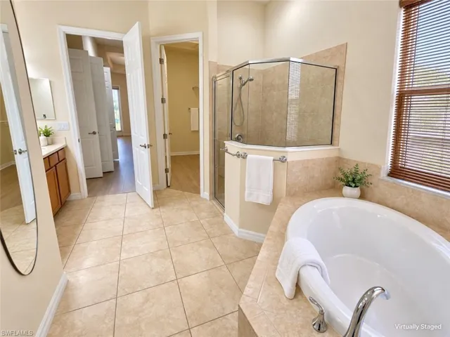 Built-in soaking tub, glass-enclosed shower, wood-finish blinds, tile flooring, and a vanity with a white countertop