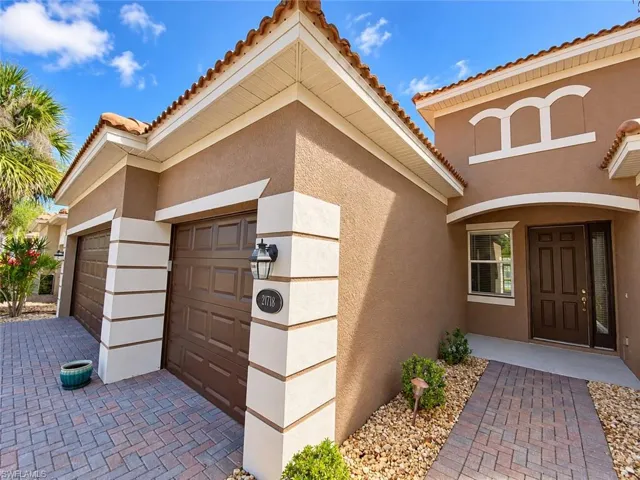 Mediterranean-style exterior featuring a tile roof, stucco finish, paver driveway, and an arched entry