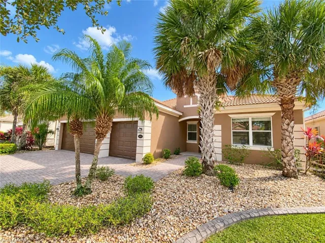 Stucco exterior residence featuring a tiled roof, paver driveway, three garage doors, and mature palm trees