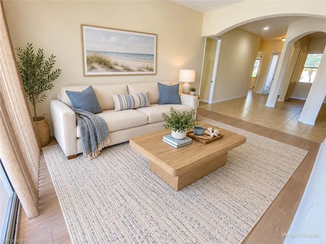 Bright living room featuring a cream upholstered sofa, wood-finish flooring throughout, neutral area rug, and an arched entryway with sidelights