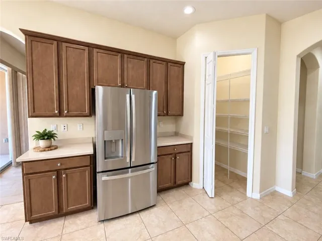 Built-in cabinetry with crown molding, stainless steel French door refrigerator, light-toned countertop, tile flooring, and a pantry with wire shelving