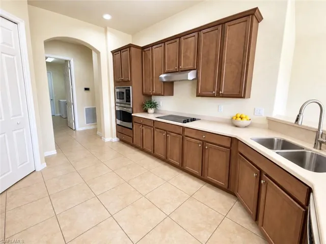 Expansive kitchen featuring wood cabinetry, light-toned countertops, a stainless steel double sink, and integrated stainless steel appliances