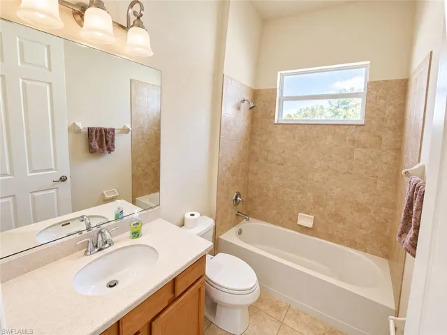 Bathroom featuring a single vanity with an integrated sink, a rectangular mirror with overhead lighting, a built-in bathtub with a shower, and full-height tiled walls