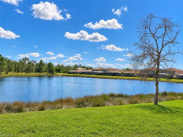 Lakeside setting featuring a tranquil body of water, extensive green lawn, and distant natural foliage