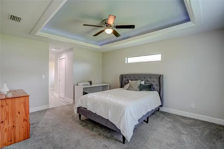 Bedroom with a tray ceiling, ceiling fan, and light colored carpet