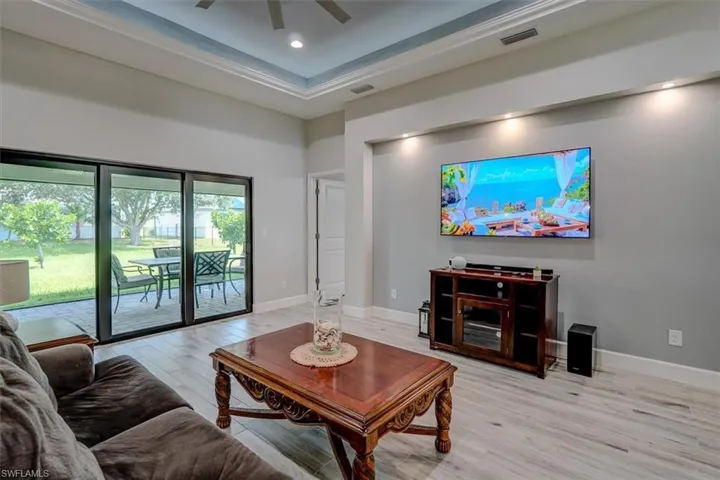Living room with ceiling fan, light hardwood / wood-style flooring, a raised ceiling, and a high ceiling