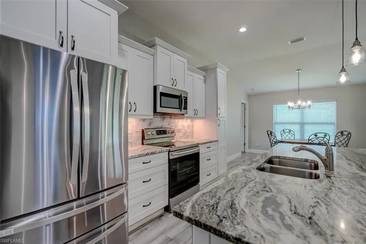 Kitchen featuring light stone counters, white cabinets, stainless steel appliances, decorative light fixtures, and sink