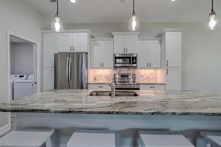 Kitchen featuring white cabinetry, appliances with stainless steel finishes, and decorative light fixtures