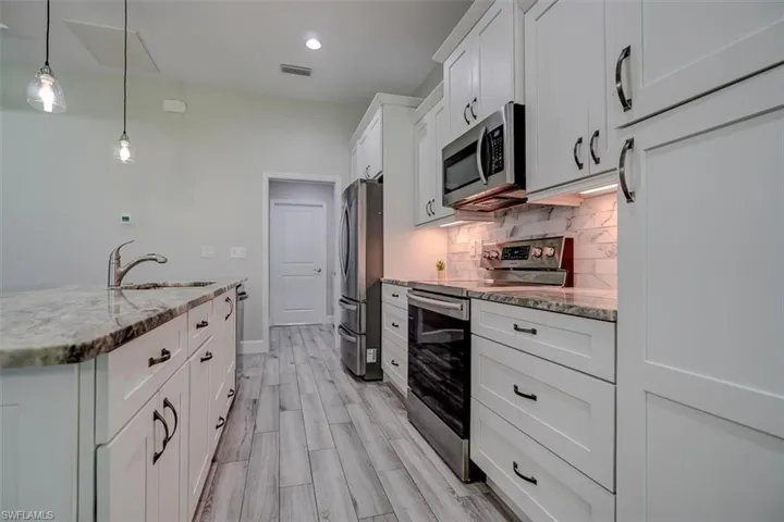 Kitchen with sink, white cabinets, appliances with stainless steel finishes, decorative light fixtures, and light stone countertops