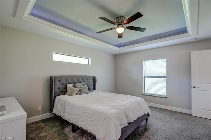 Bedroom featuring ceiling fan, a raised ceiling, and dark colored carpet