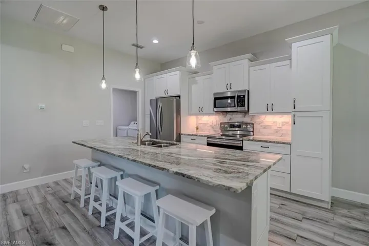 Kitchen with white cabinets, a kitchen island with sink, stainless steel appliances, and decorative light fixtures