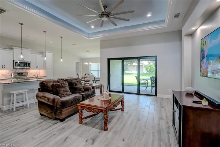 Living room with light hardwood / wood-style tile flooring, a tray ceiling, and ceiling fan
