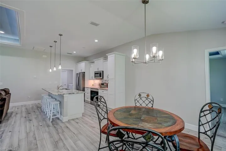 Dining area with vaulted ceiling, sink, light wood-type flooring, and a chandelier