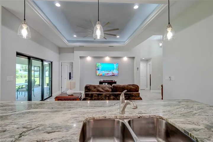 Kitchen with a tray ceiling, sink, ceiling fan, and light stone counters