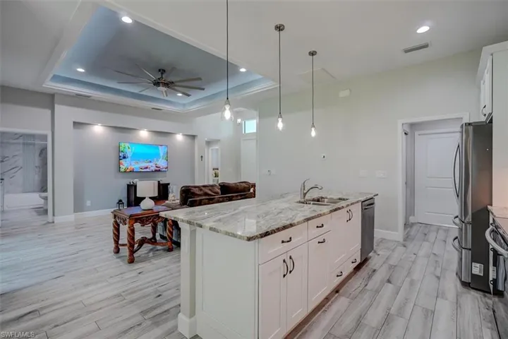Kitchen featuring appliances with stainless steel finishes, white cabinetry, a raised ceiling, light stone countertops, and decorative light fixtures