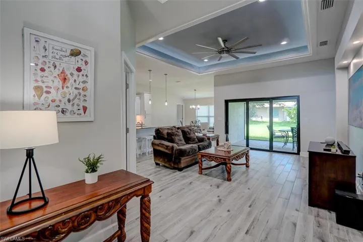 Living room with a raised ceiling, light hardwood / wood-style tile flooring, and ceiling fan with notable chandelier