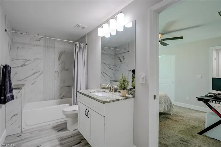 Full bathroom with ceiling fan, vanity, wood-type flooring, toilet, and shower / tub combo with curtain