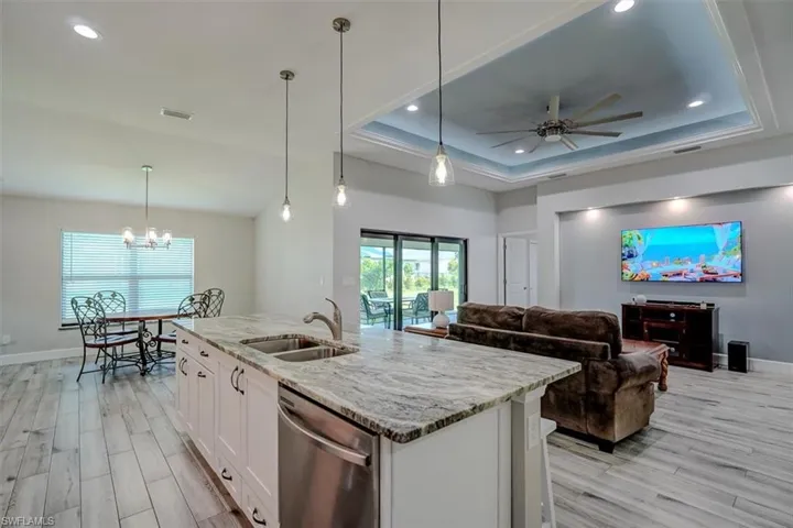 Kitchen with white cabinetry, light stone counters, dishwasher, pendant lighting, and sink