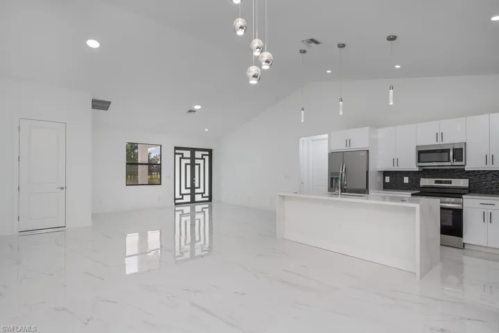 Kitchen with a center island with sink, decorative light fixtures, stainless steel appliances, backsplash, and white cabinets