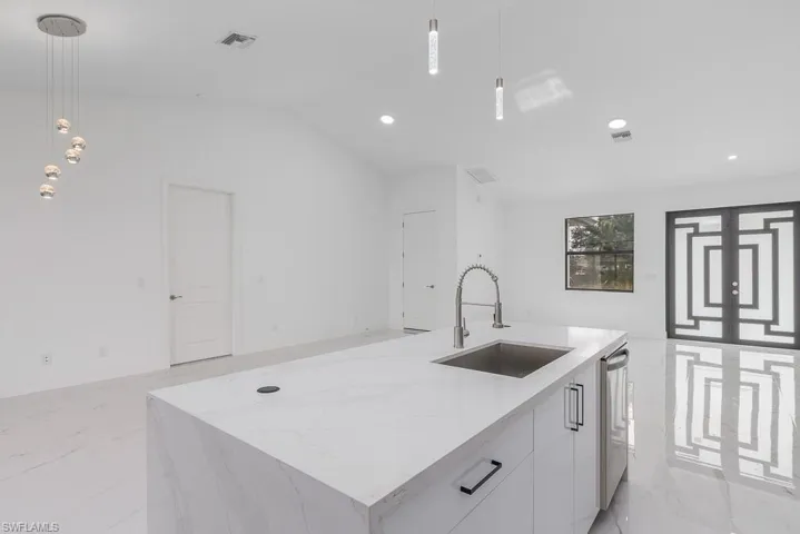 Kitchen featuring decorative light fixtures, a center island with sink, sink, and white cabinetry