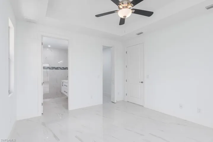 Unfurnished bedroom featuring ceiling fan, a raised ceiling, and connected bathroom