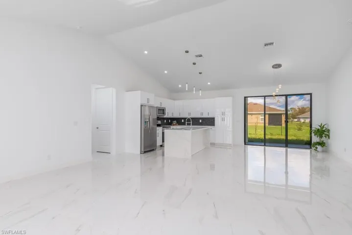 Kitchen featuring decorative light fixtures, a kitchen island with sink, appliances with stainless steel finishes, and white cabinetry