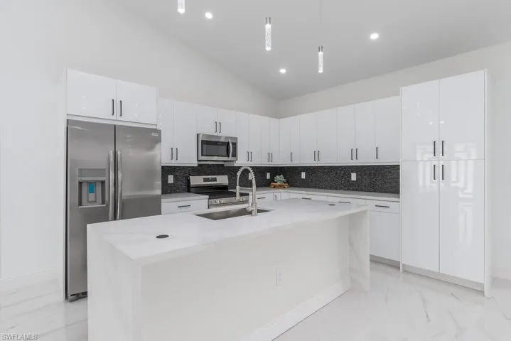 Kitchen featuring a kitchen island with sink, sink, high vaulted ceiling, appliances with stainless steel finishes, and white cabinetry