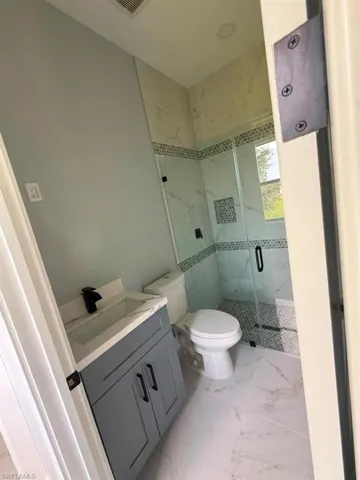 Bathroom featuring a gray vanity with a white countertop and black fixtures, a white toilet, and a glass-enclosed shower