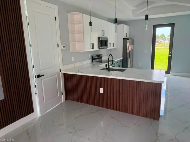 Modern kitchen featuring a waterfall island with wood slat paneling, quartz countertops, white cabinetry, stainless steel appliances, and large format porcelain tile flooring