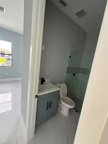 Compact bathroom featuring a glass-enclosed shower with decorative accent tiling, a single vanity with a blue cabinet, and a black faucet