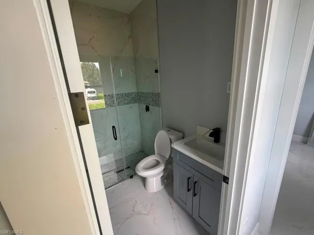 Bathroom featuring a glass-enclosed shower with tile surround, a single vanity with a gray cabinet and white countertop, and contemporary black fixtures