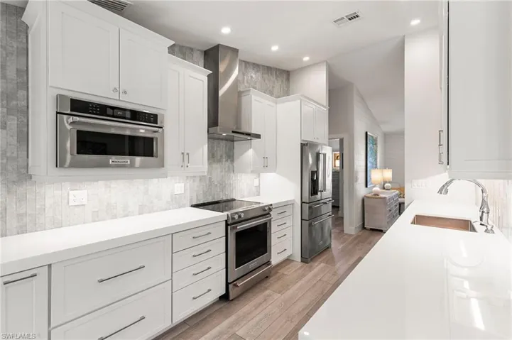 Kitchen with stainless steel appliances, wall chimney range hood, white cabinetry, backsplash, and recessed lighting
