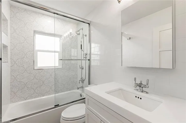 Full bath featuring combined bath / shower with glass door, vanity, tile walls, and tasteful backsplash