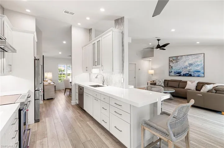 Kitchen with open floor plan, stainless steel appliances, ceiling fan, white cabinets, and a kitchen bar