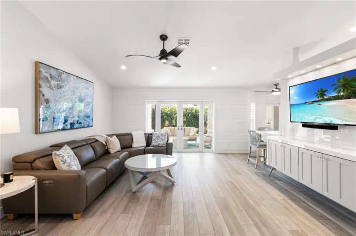 Living room featuring light wood-style flooring, ceiling fan, french doors, wood walls, and recessed lighting