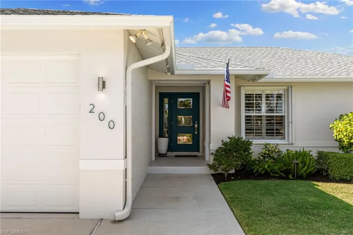 Entrance to property featuring a shingled roof, stucco siding, and a lawn