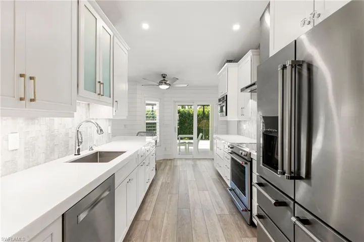 Kitchen with appliances with stainless steel finishes, white cabinetry, recessed lighting, light stone counters, and light wood-style floors