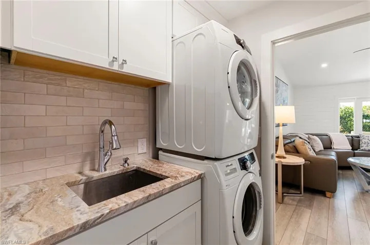 Washroom featuring light wood-type flooring, stacked washer / drying machine, and cabinet space