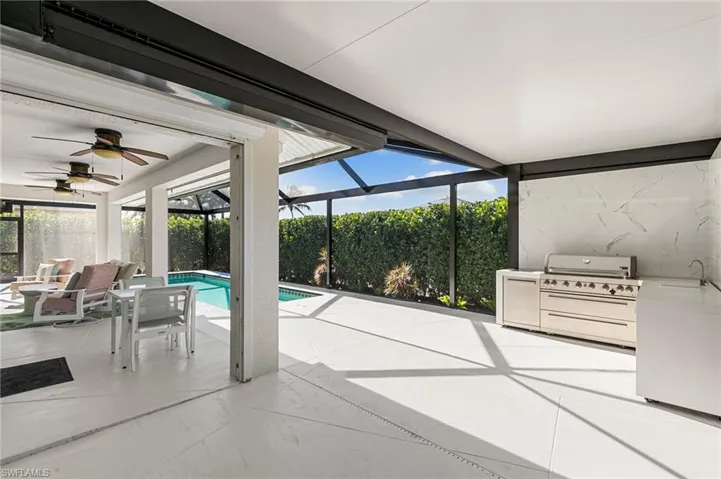 View of pool featuring glass enclosure, a sunroom, a patio area, and an outdoor kitchen