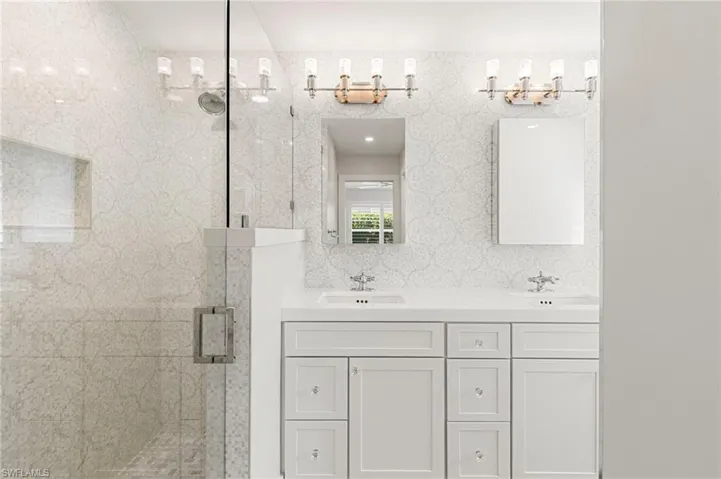 Full bath with double vanity and a marble finish shower